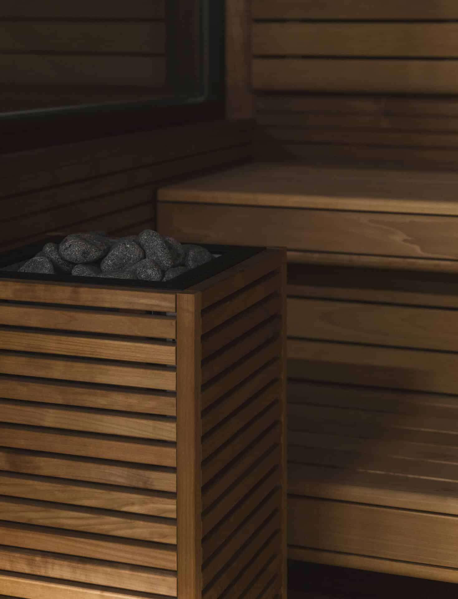 HUUM CORE sauna heater with dark wood slats and exposed stones beside tiered wooden benches