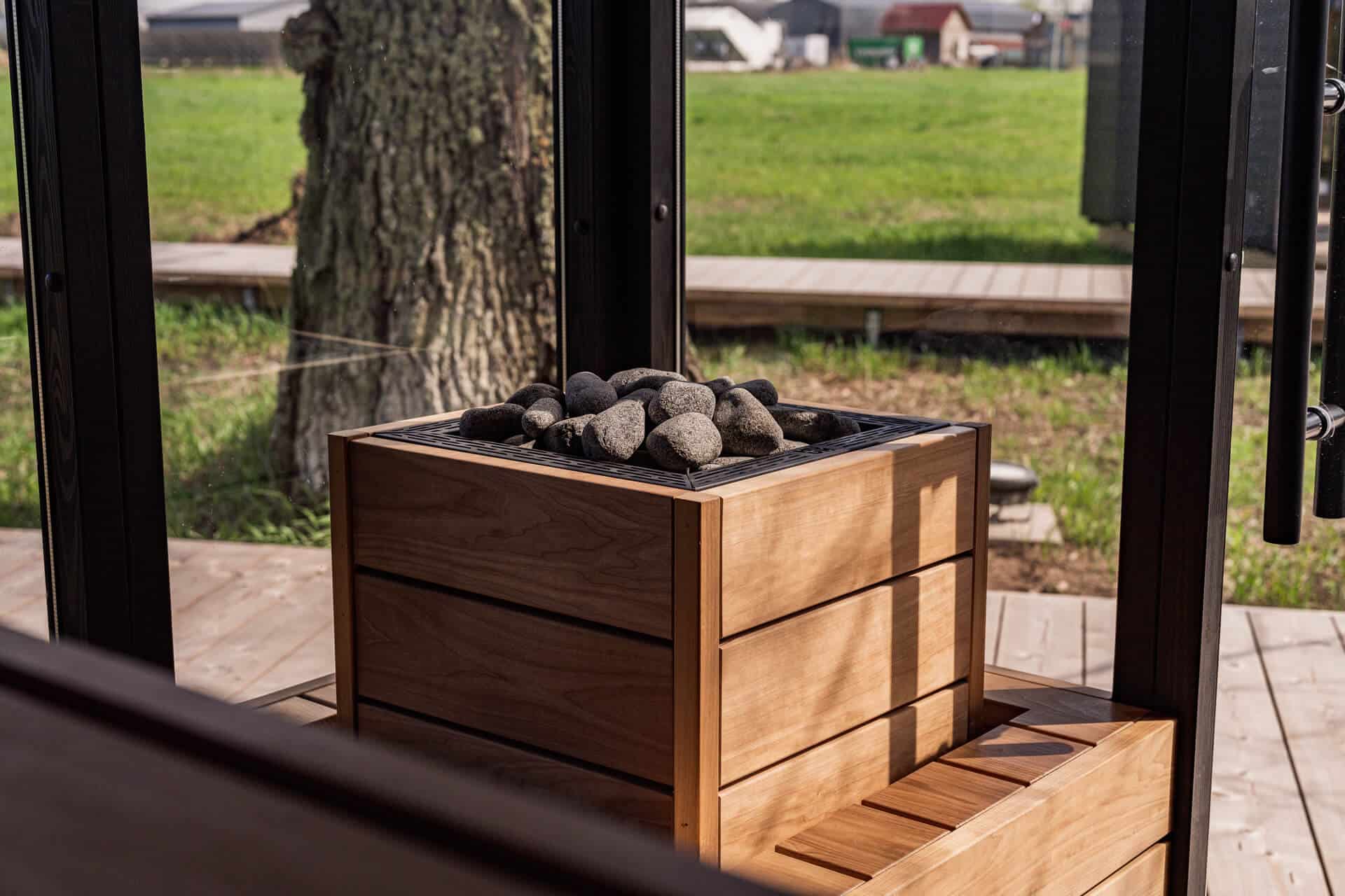 HUUM CORE sauna heater with broad wood panels and exposed stones beside a window overlooking grass
