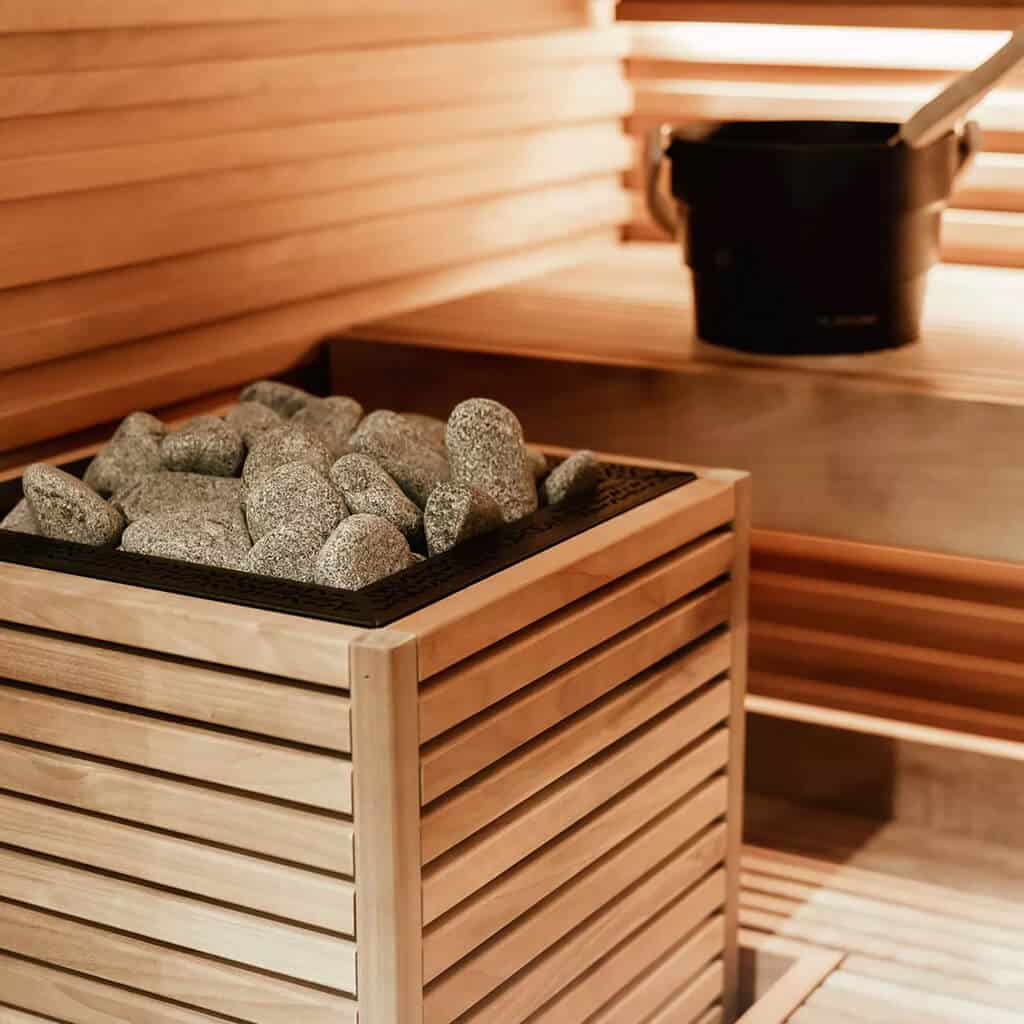HUUM CORE sauna heater with wood slats and exposed stones beside a bench with a black bucket