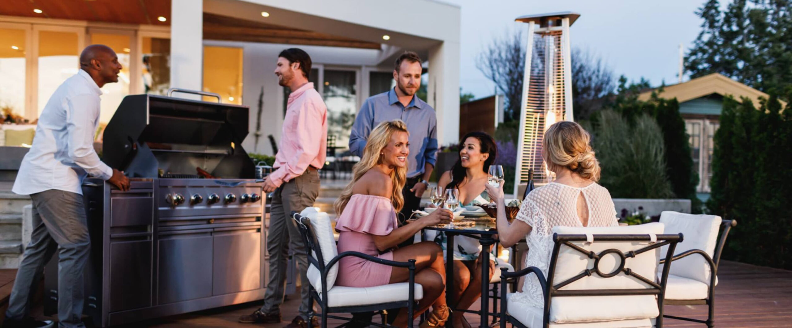 Friends gathered on a patio beside a Crown Verity stainless steel outdoor kitchen grill